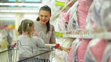 美丽美丽的母亲，黑发正在为她的女儿展示粉红枕头站在<strong>超市货架</strong>附近。